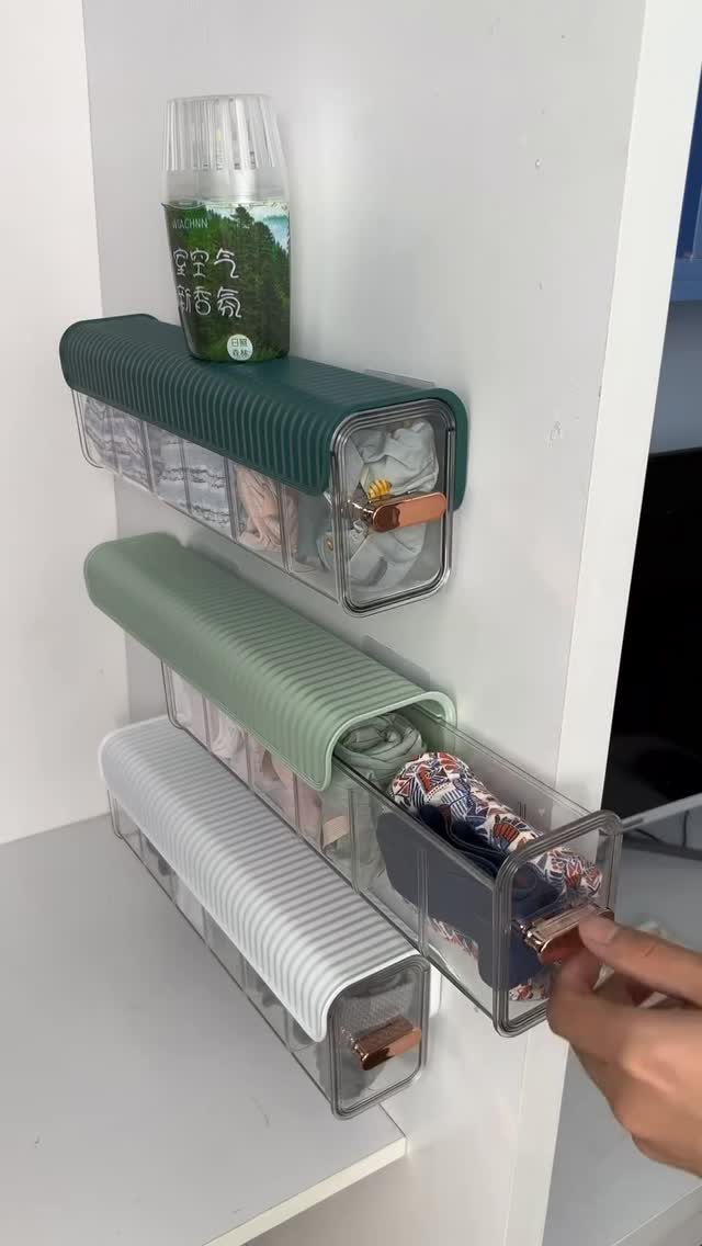 Clear wall-mounted mini drawers with ribbed covers holding small fabric items on white wall