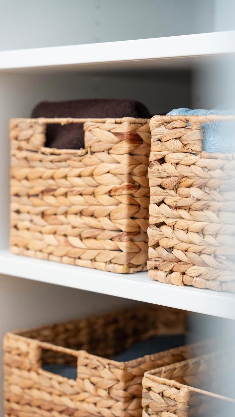 Woven wicker baskets with folded clothes on white closet shelves for organization.