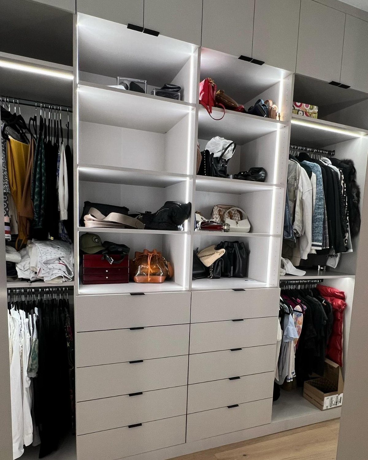 White built-in closet system with integrated LED lighting under shelves and hanging clothes.