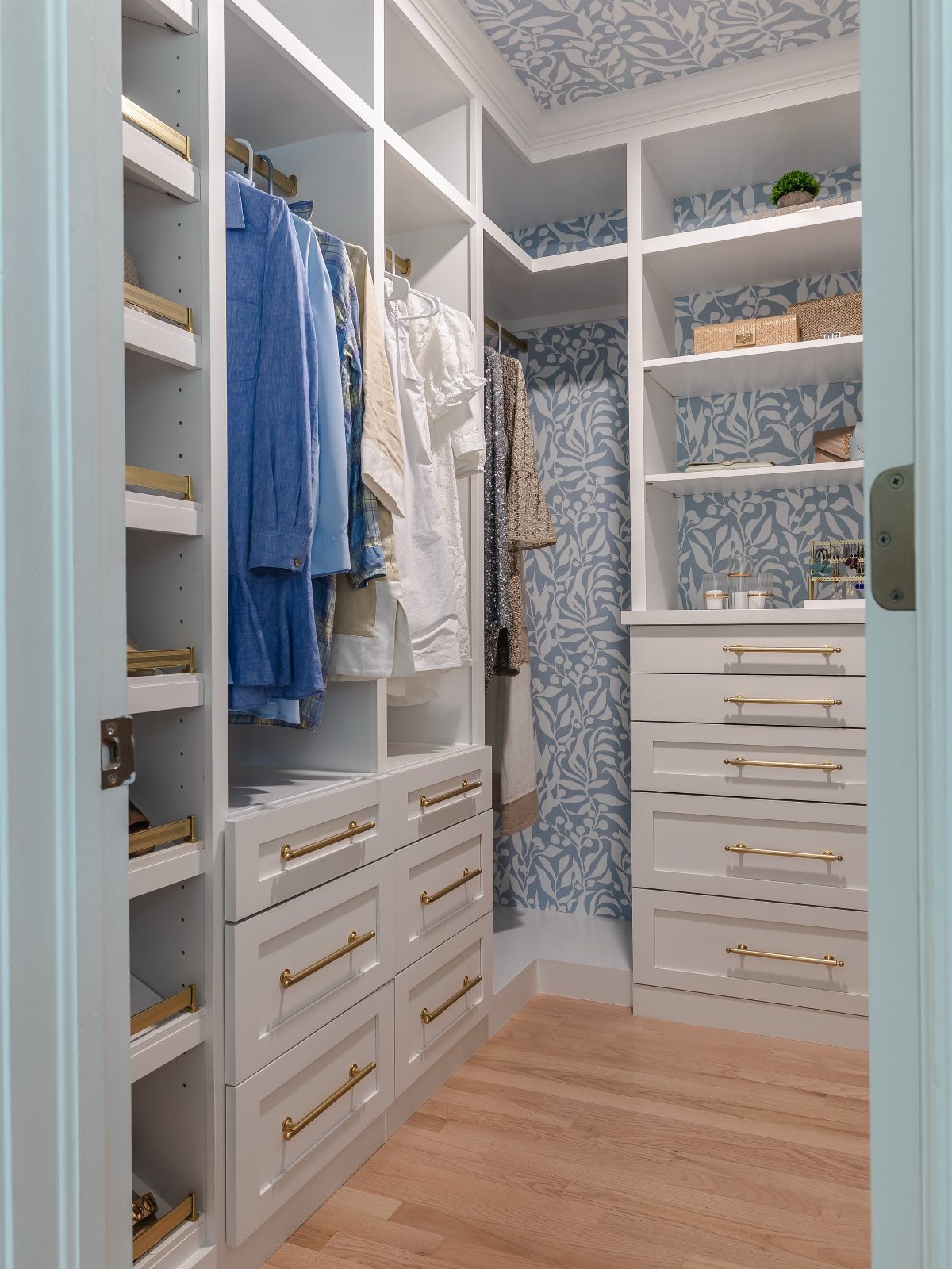 White built-in closet with blue and white leaf-patterned wallpaper on the back wall.