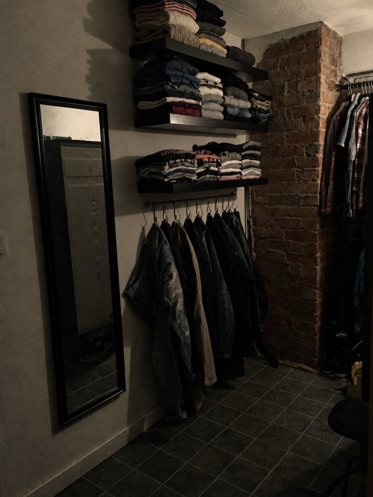 Black floating shelves with folded clothes above a rod of hanging jackets.