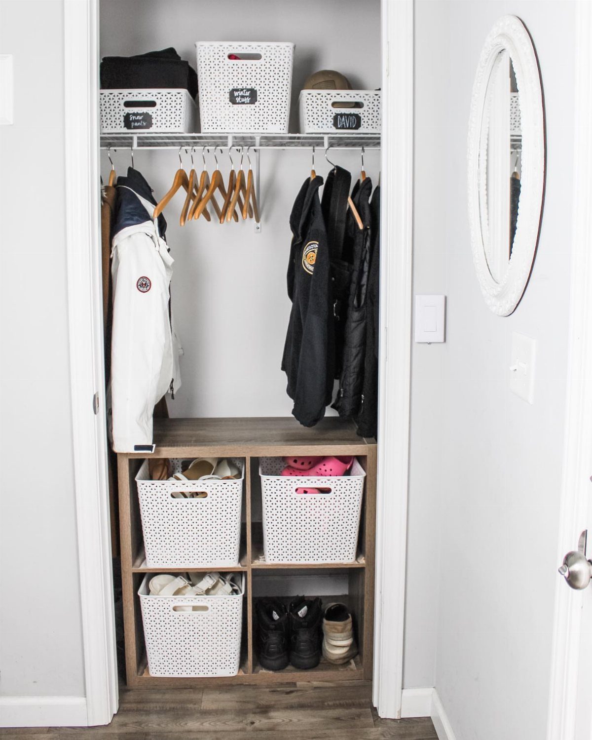 White perforated storage bins organized in a closet with a wooden cube shelf.