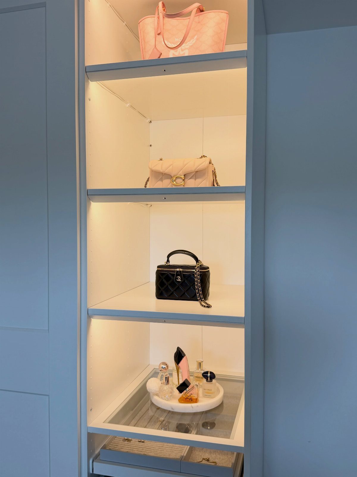 Narrow built-in closet shelving unit organizing handbags and perfume bottles in a small space.
