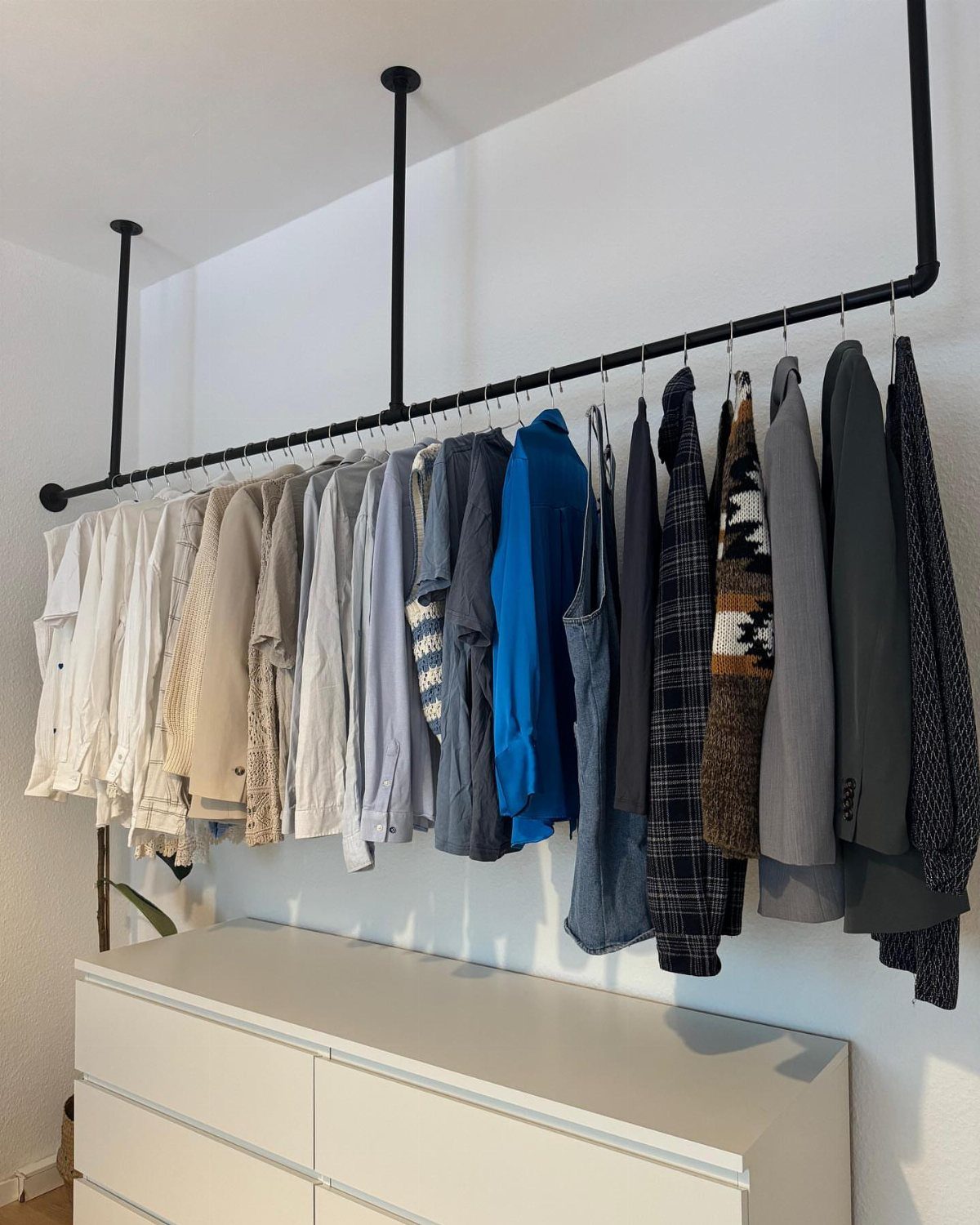 Black industrial clothing rod with hanging shirts above a white dresser.