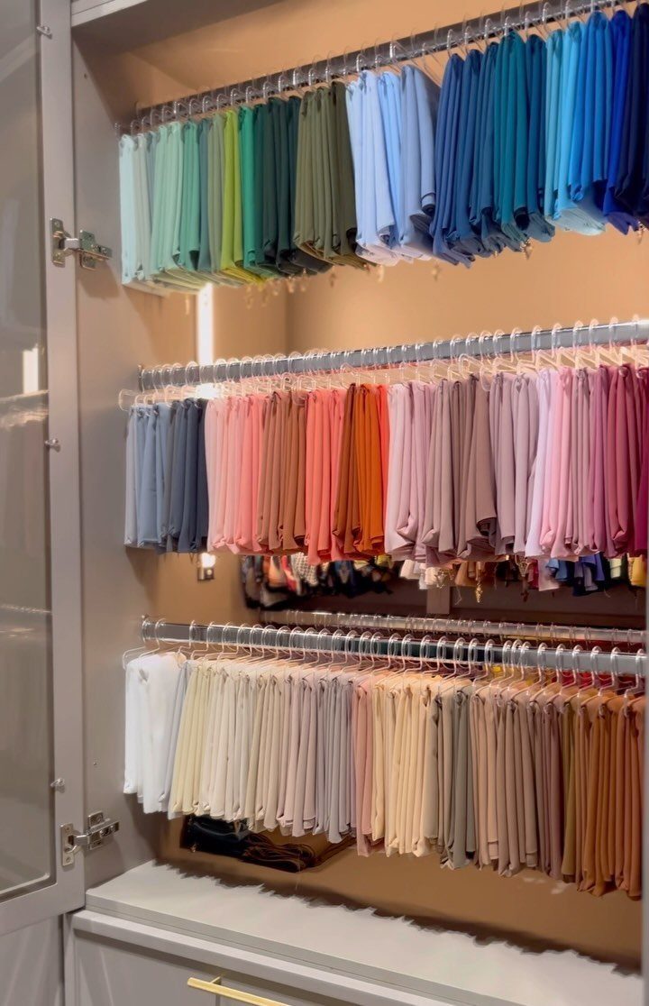 Three tiers of colorful clothes organized by color on hanging rods in a closet.