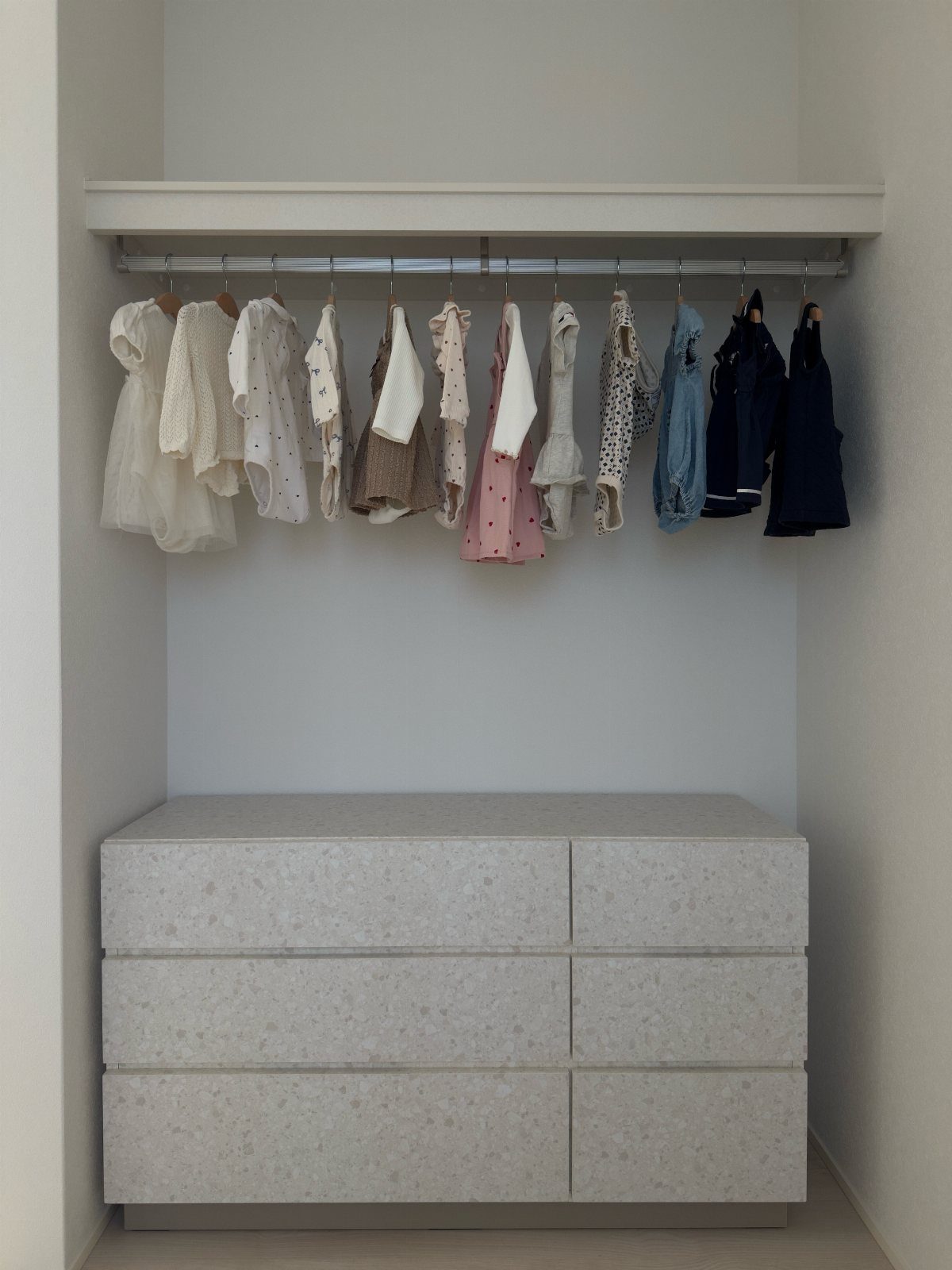 White dresser with drawers placed inside a closet beneath a hanging rod.