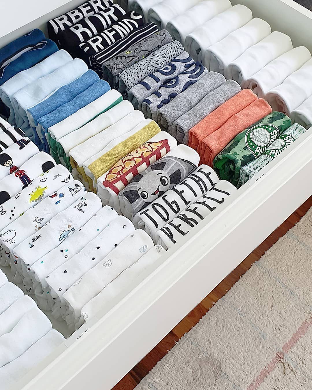 Neatly file-folded children's clothes arranged in upright rows inside a white dresser drawer.
