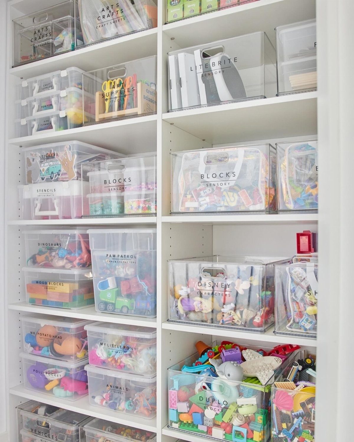 Clear plastic bins with labels organizing colorful toys on white closet shelves.