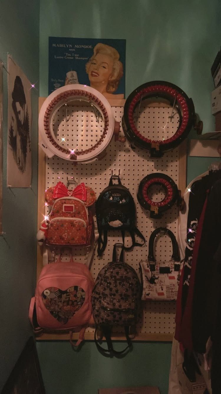 White pegboard with hooks holding various backpacks and handbags on a blue wall.