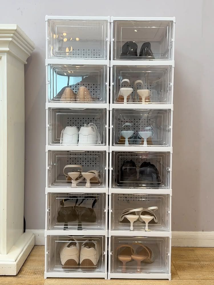 Clear plastic shoe organizer bins stacked vertically containing various women's footwear on wood flooring.