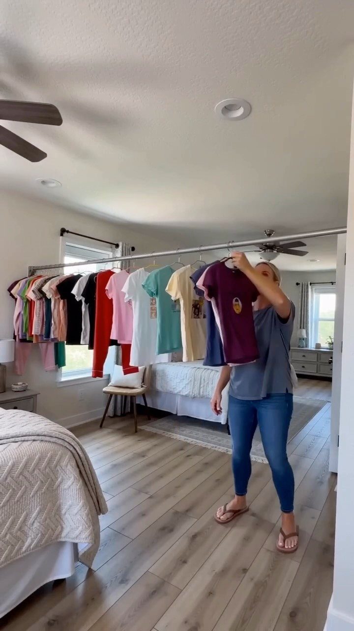 Woman selecting a purple shirt from a wall-mounted clothing rack in a bedroom.