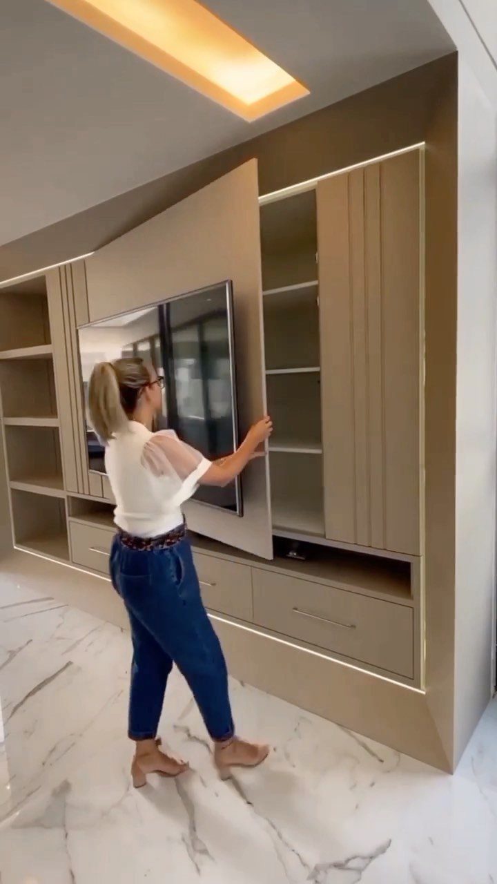 Woman opening a sliding panel to reveal concealed wall cabinetry in a living room.