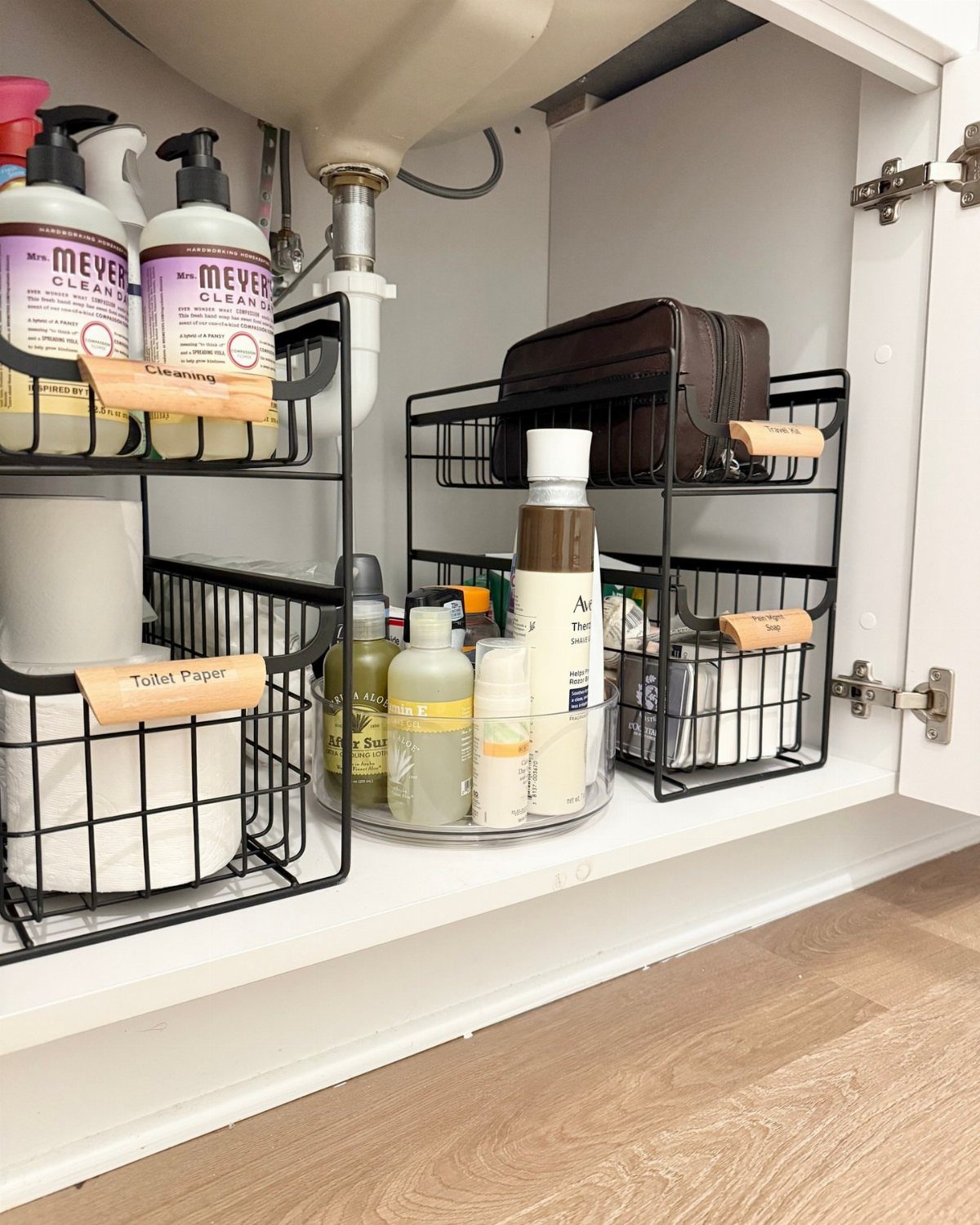 Bathroom under-sink cabinet with black wire organizers holding cleaning supplies and toiletries.