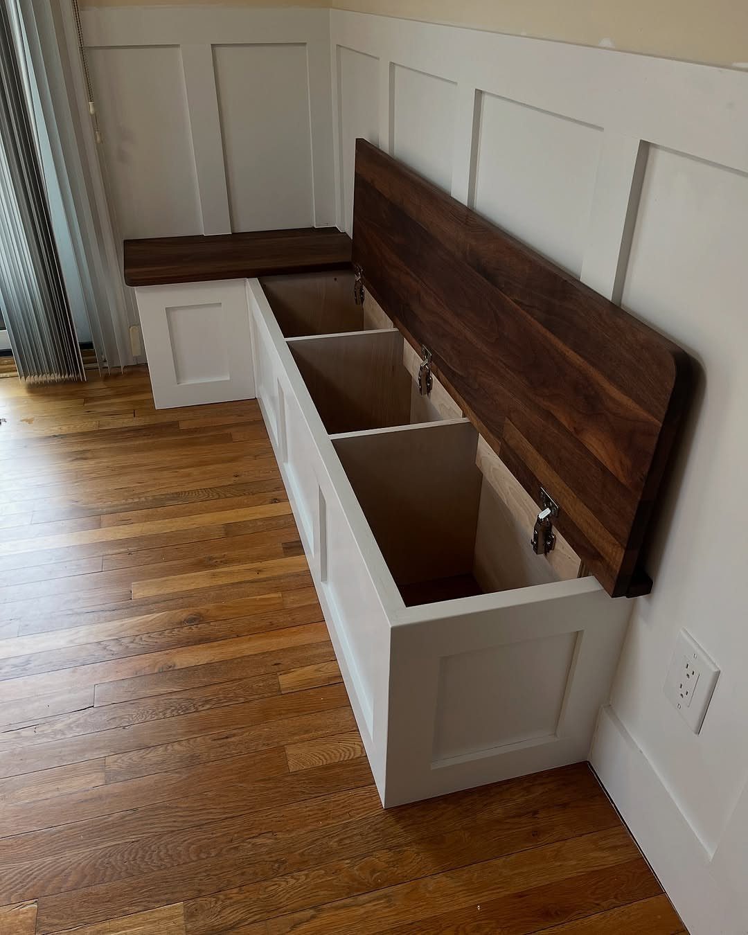 White built-in storage bench with dark wood lid open to show interior compartments.