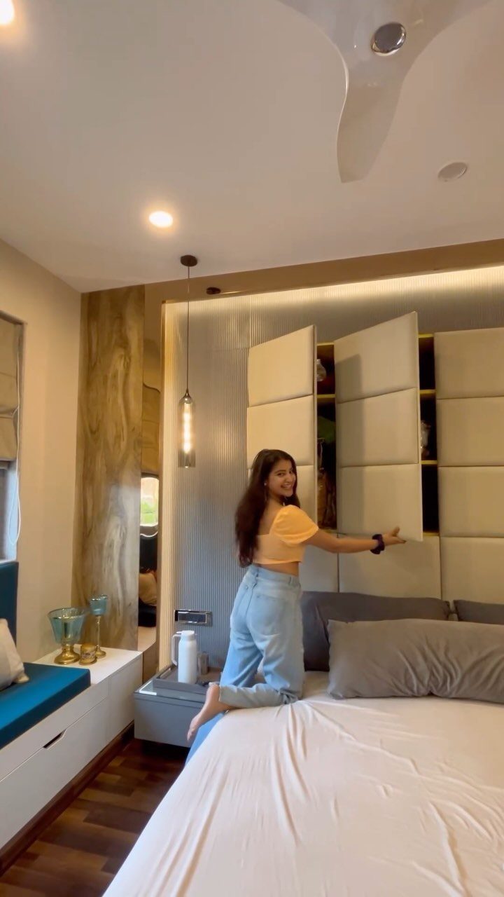 Woman opening a concealed storage compartment in a padded wall headboard above a bed