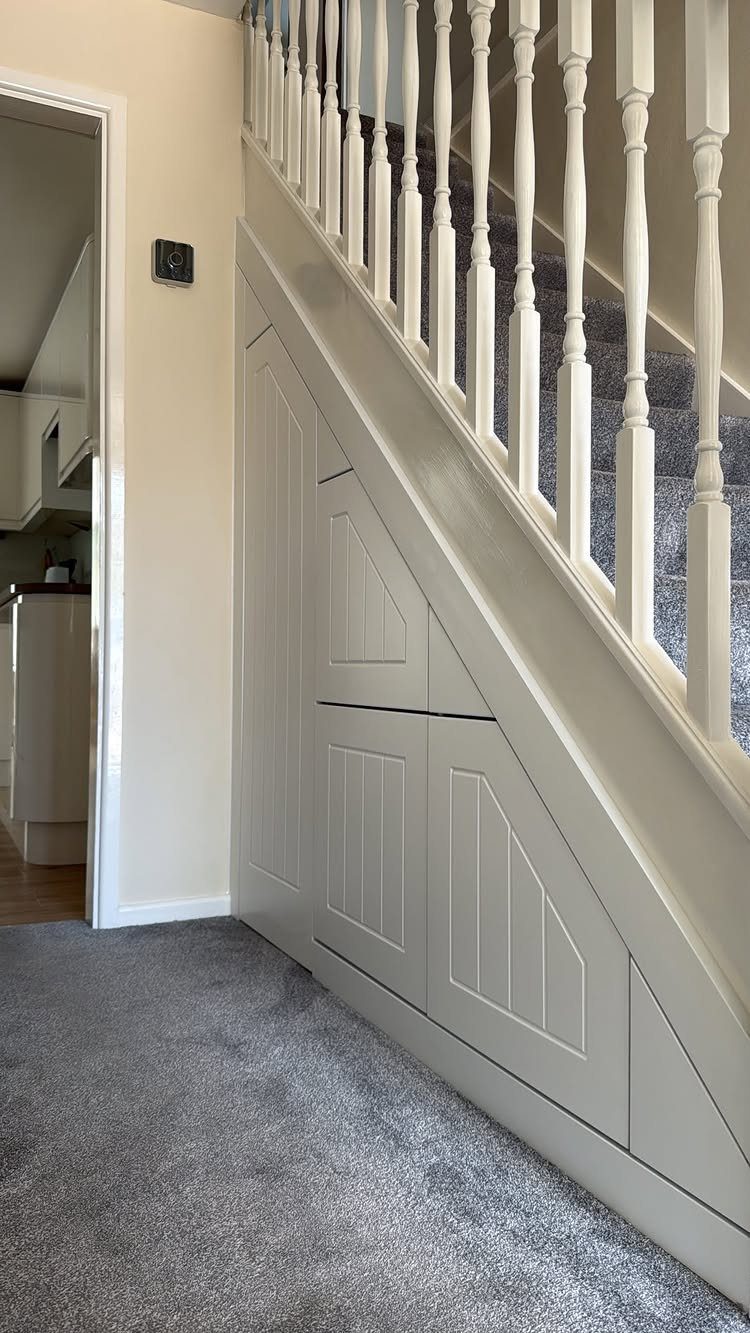 Built-in grey storage cabinets installed under a white staircase with a grey carpeted floor.