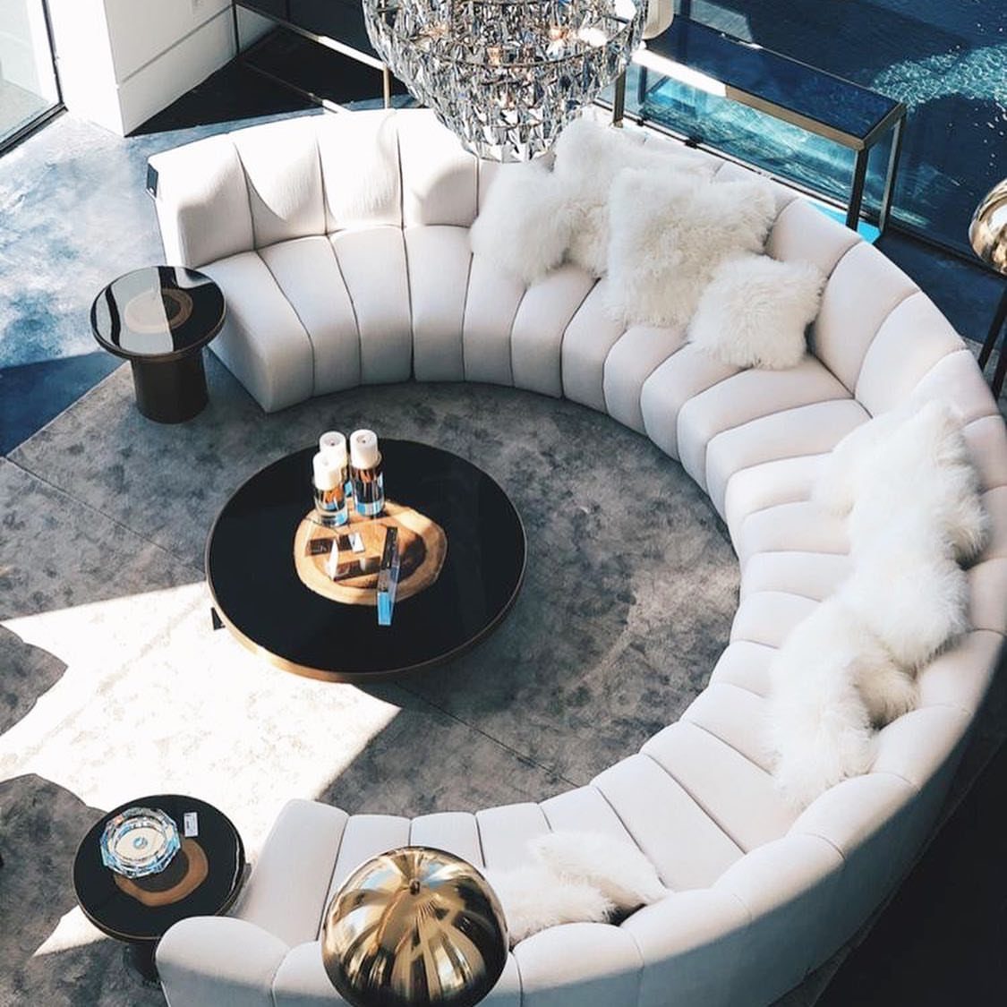 Curved white sectional sofa surrounding a round black coffee table on a grey rug.
