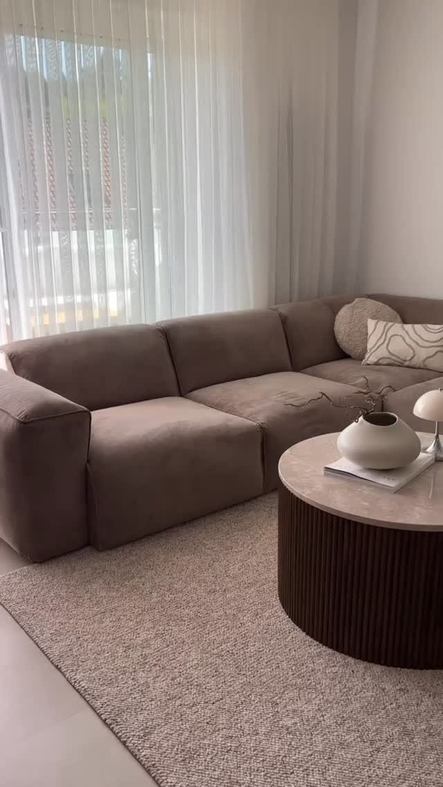 Brown L-shaped corner sofa with a round coffee table on a beige rug.