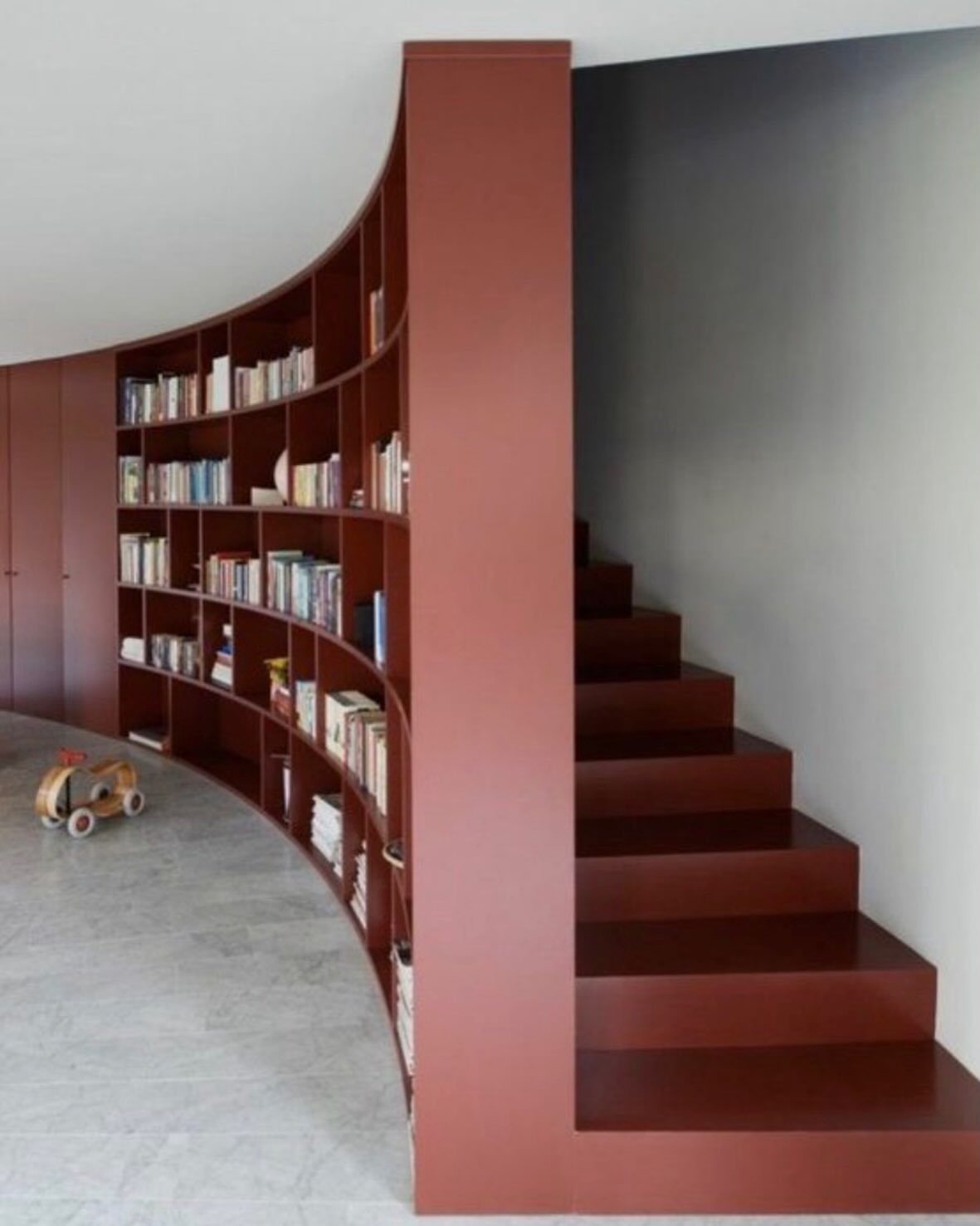 Curved reddish-brown built-in bookshelves integrated into the side of a matching staircase.