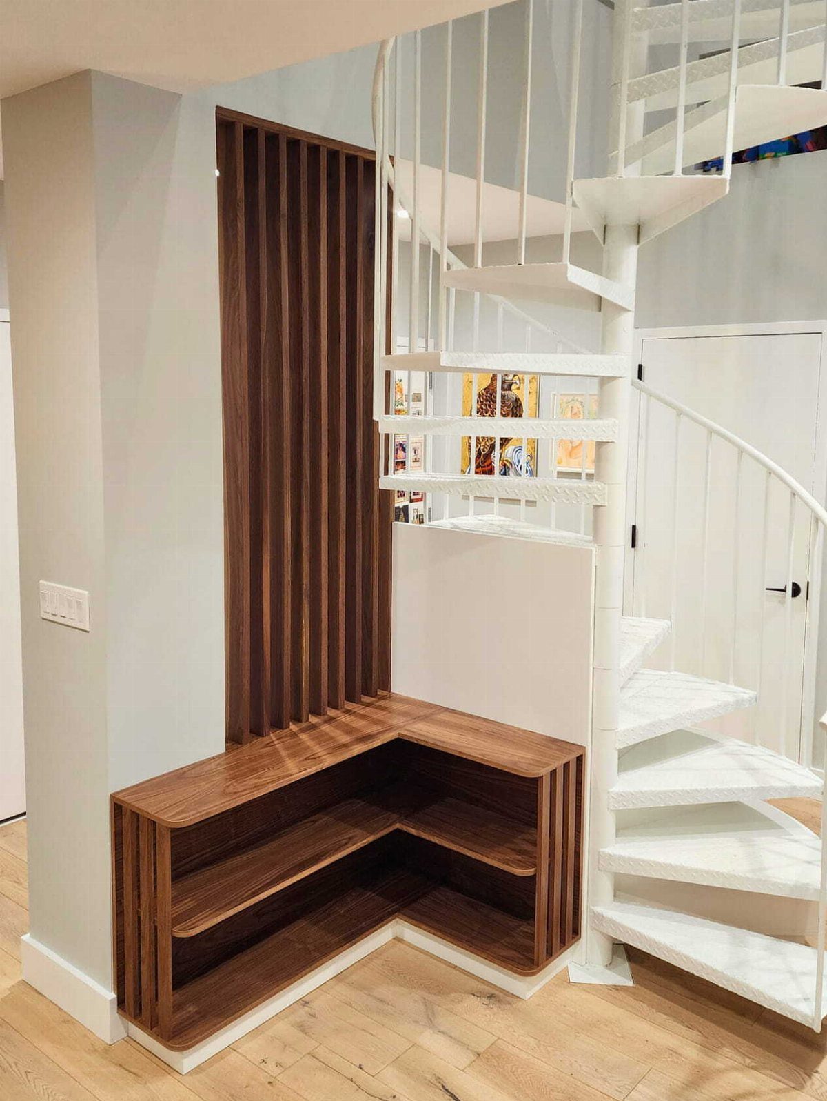 Custom wooden L-shaped storage unit and slatted wall beside a white spiral staircase.