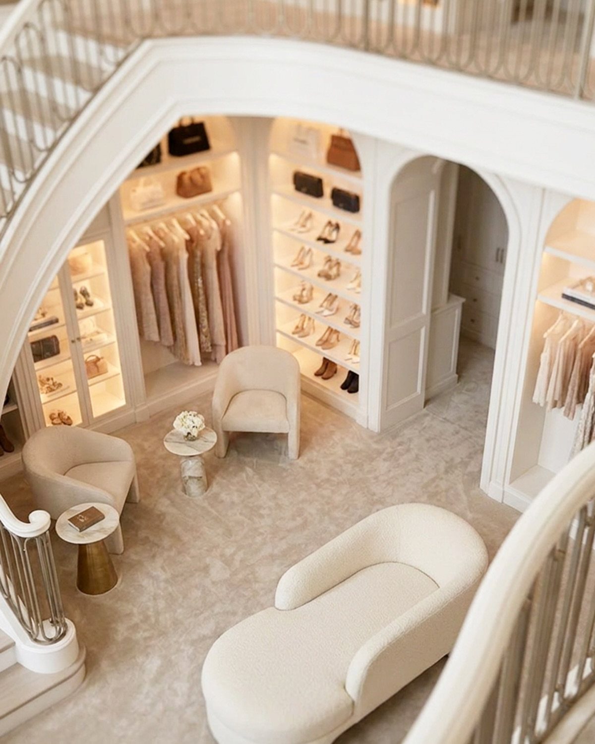 Luxurious white walk-in closet with shelving and seating built under a curved staircase.