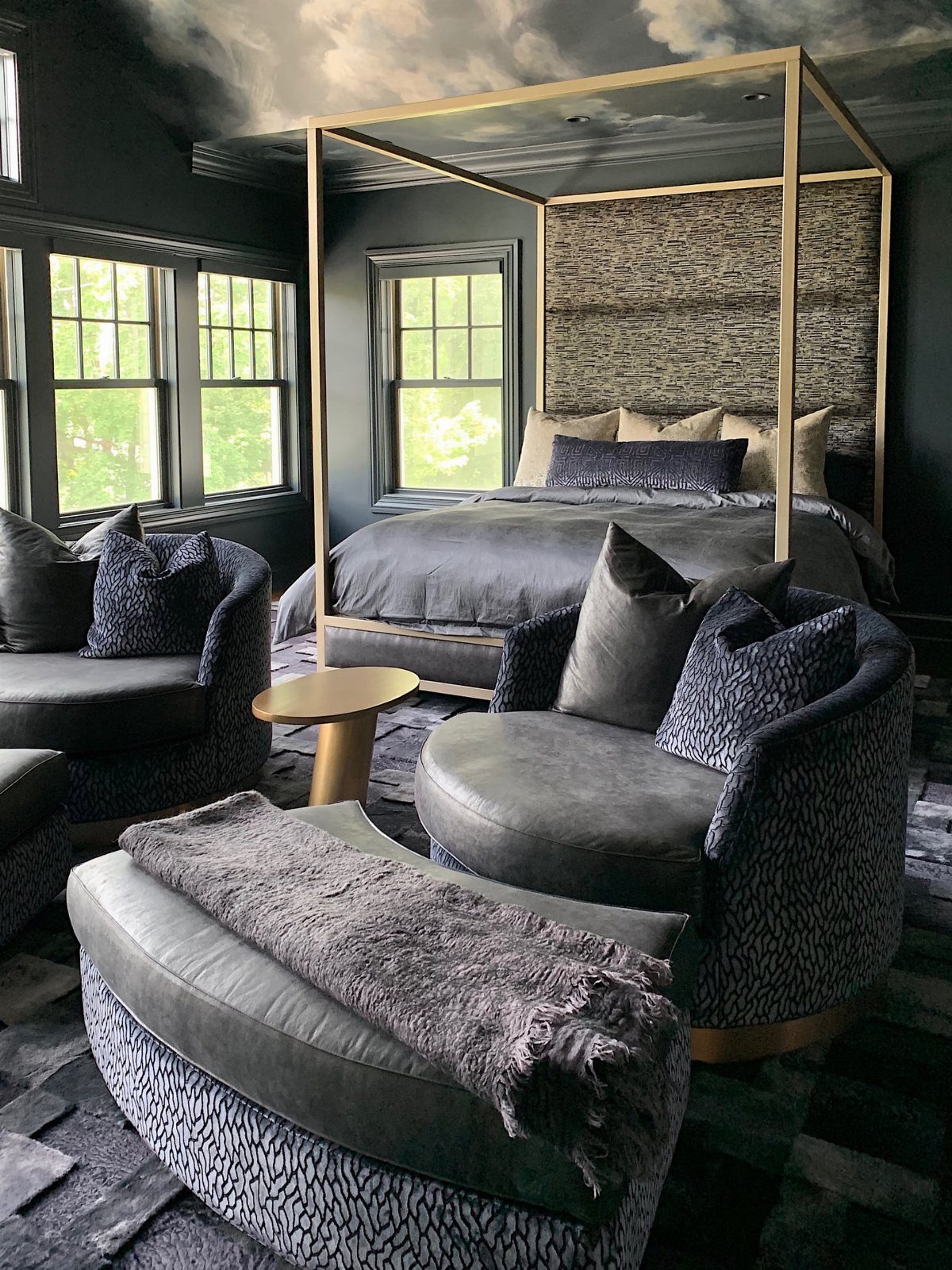 Gold canopy bed in a dark moody bedroom with grey furniture and cloud ceiling.