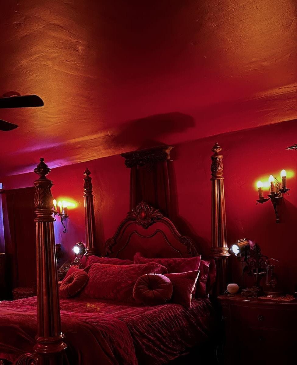 Four-poster bed with red bedding and warm wall-mounted candle sconces in a red room.