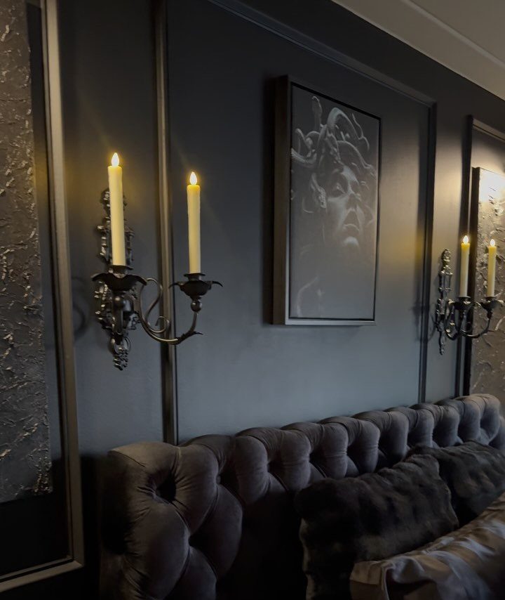 Grey tufted velvet headboard against a black wall with ornate candle sconces.