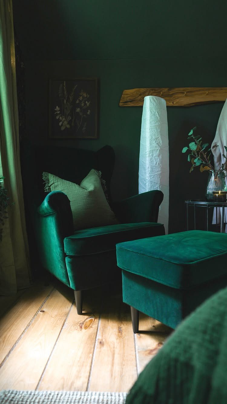 Dark green velvet armchair and ottoman against deep green walls in a moody room