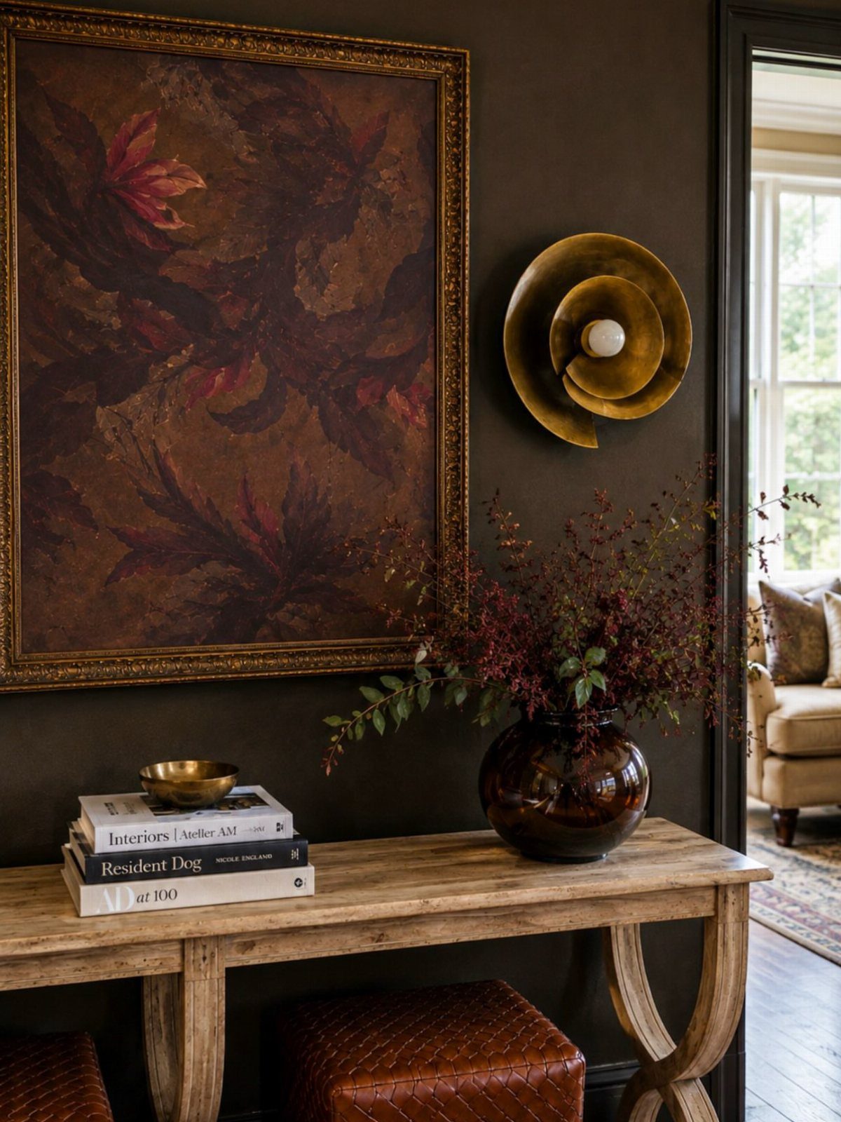 Light wood console table against a dark brown wall with gold decor and artwork