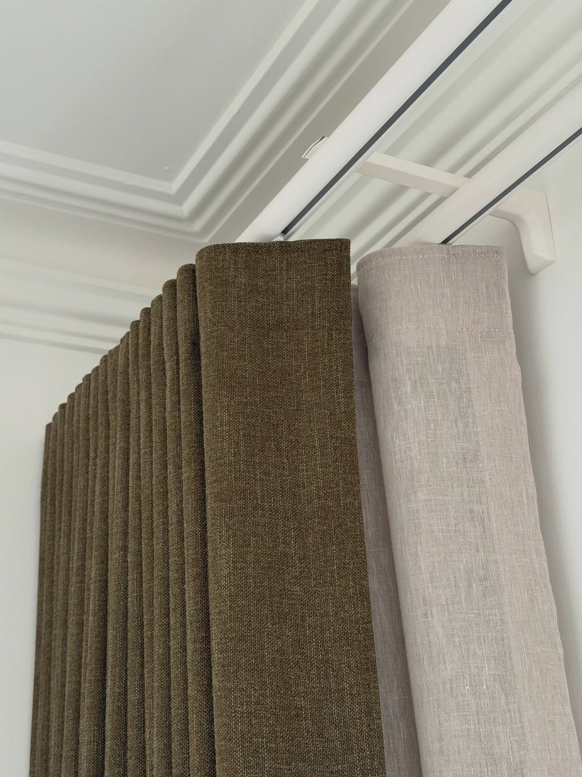 Olive green and light grey double layered curtains hanging from white rods.