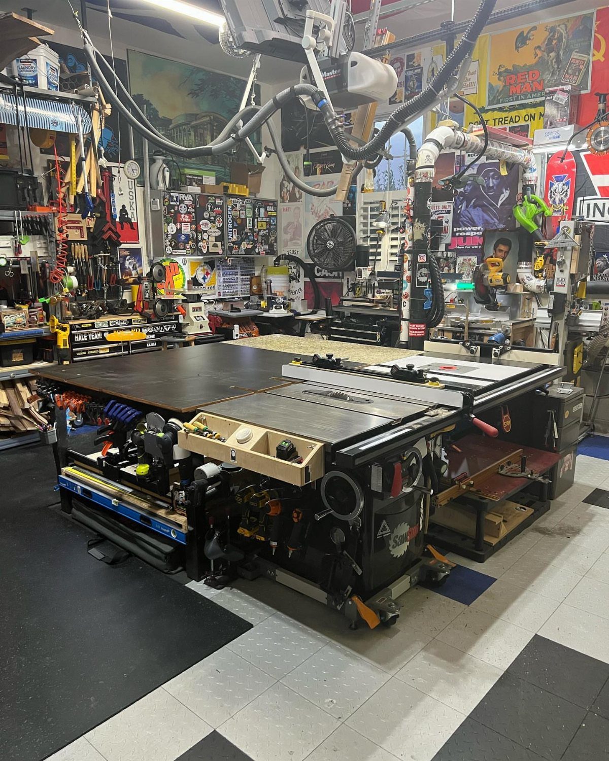 Large black workbench with an integrated table saw in a tool-filled garage workshop.