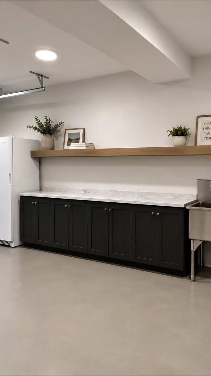 Black cabinets with marble countertop, white refrigerator and sink in a garage kitchenette.