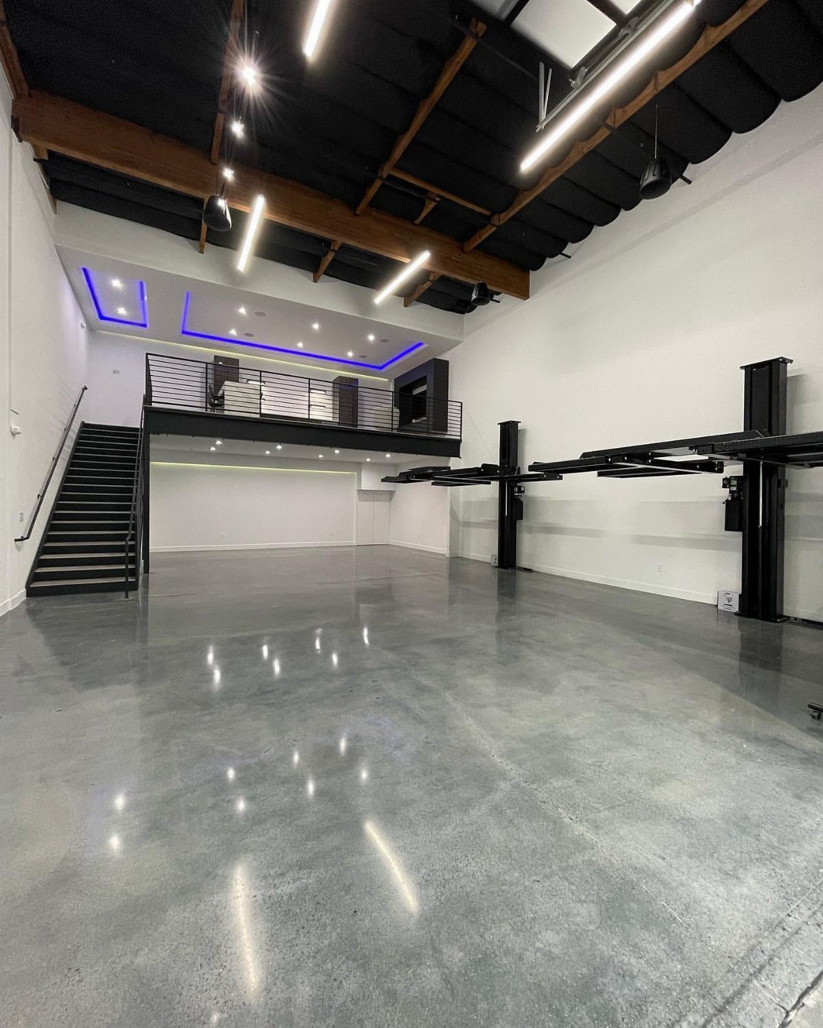 Modern garage with polished concrete floors, car lifts, and a black loft area.