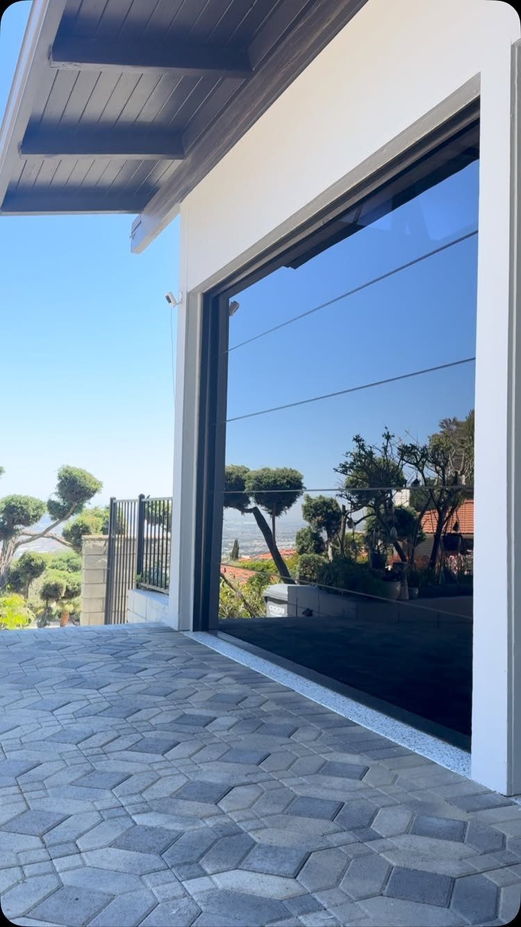 Modern glass garage door reflecting trees and sky next to hexagonal paved driveway.