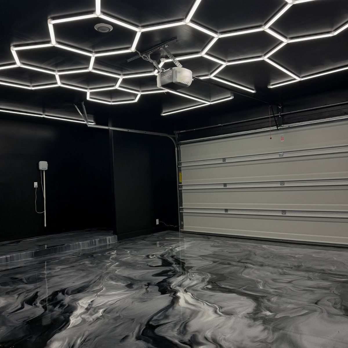 Modern garage with black walls, swirling metallic floor, and hexagonal LED ceiling lights.