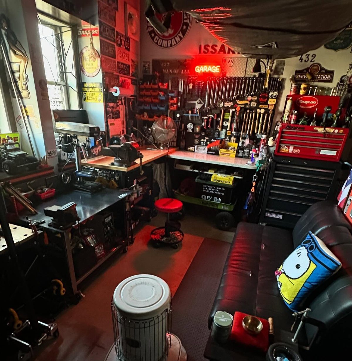 Garage workshop with red tool chests, workbenches, and a black leather lounge sofa.