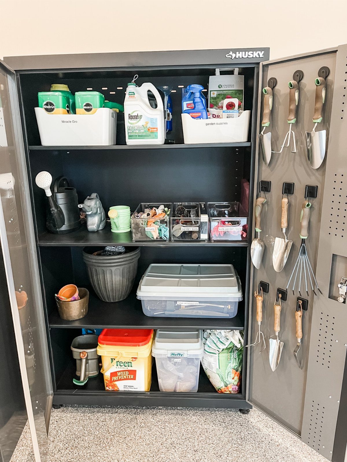 Grey metal storage cabinet with garden tools hanging on the inside door and shelves.