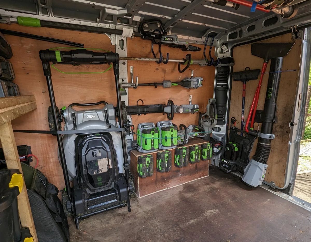 Organized garden power tools and a lawnmower inside the back of a white van.
