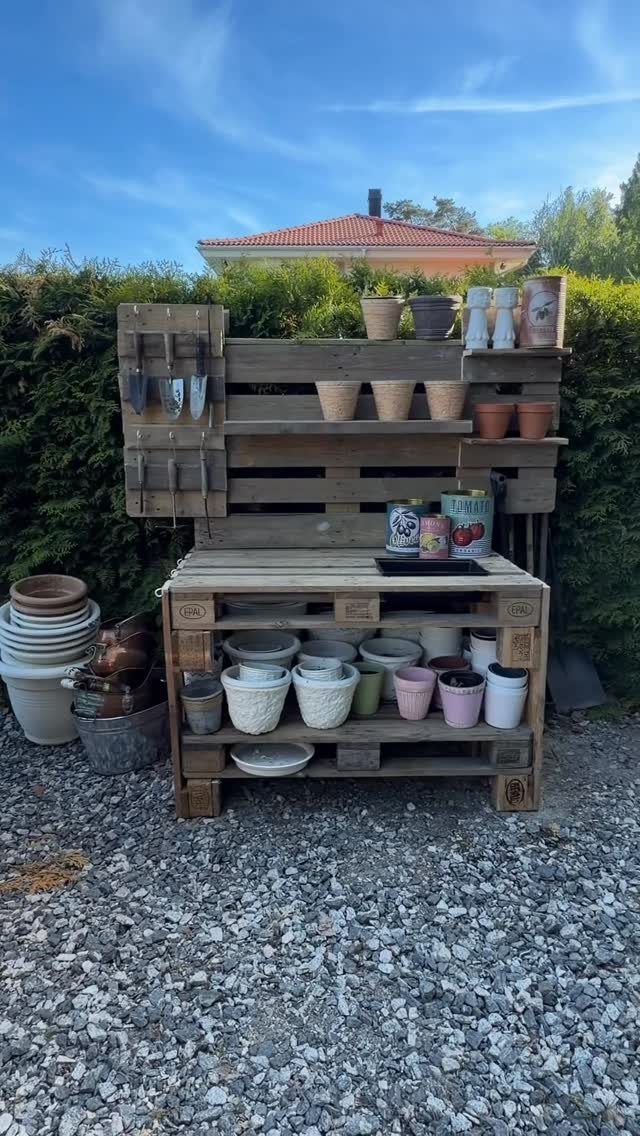 Wooden pallet shelving unit holding various ceramic and terracotta flower pots outdoors.