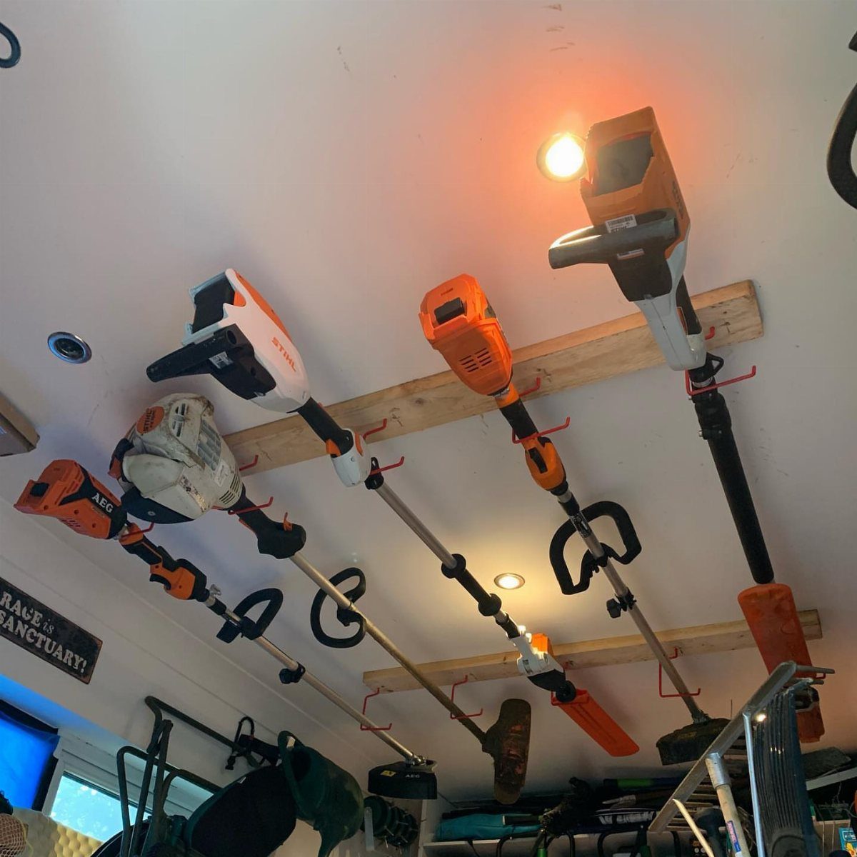 Power garden tools hanging from wooden beams and red hooks on a white ceiling.