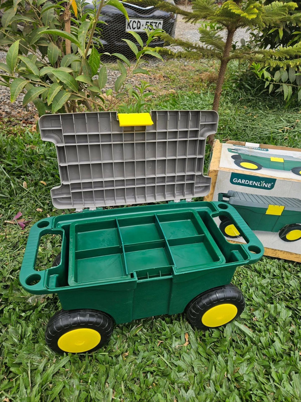 Green plastic rolling garden tool organizer with compartments and yellow wheels on grass.