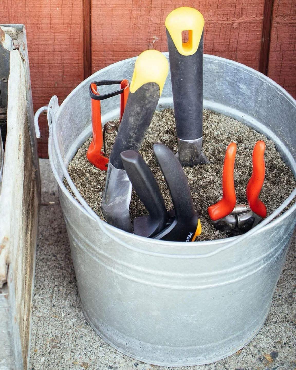 Garden hand tools stored upright in a metal bucket filled with sand.