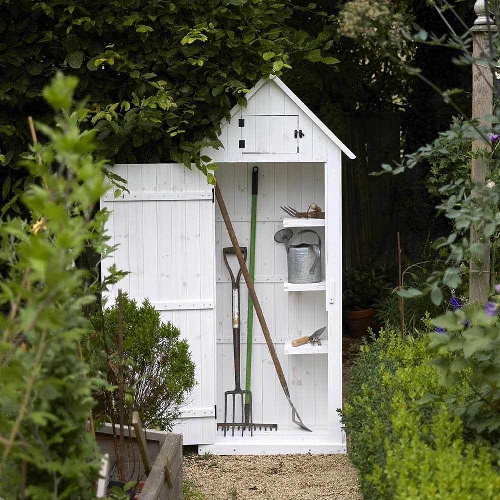Small white wooden garden storage shed containing various long-handled tools and a watering can.