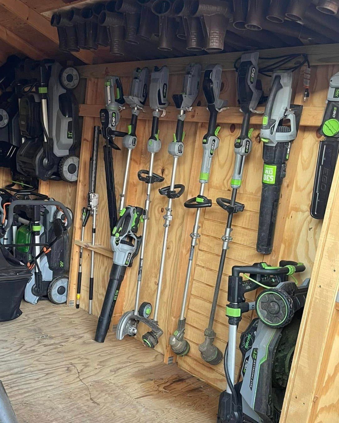 Power garden tools organized vertically on a wooden wall inside a storage shed.