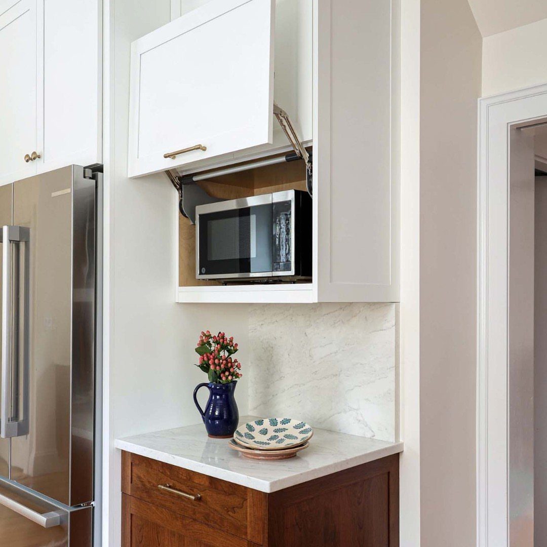 Microwave hidden inside a white lift-up kitchen cabinet above a marble countertop.