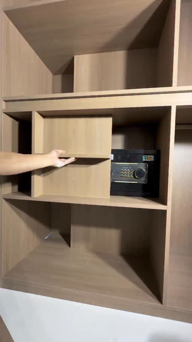 Hand sliding open a wooden panel to reveal a hidden black safe in shelving.