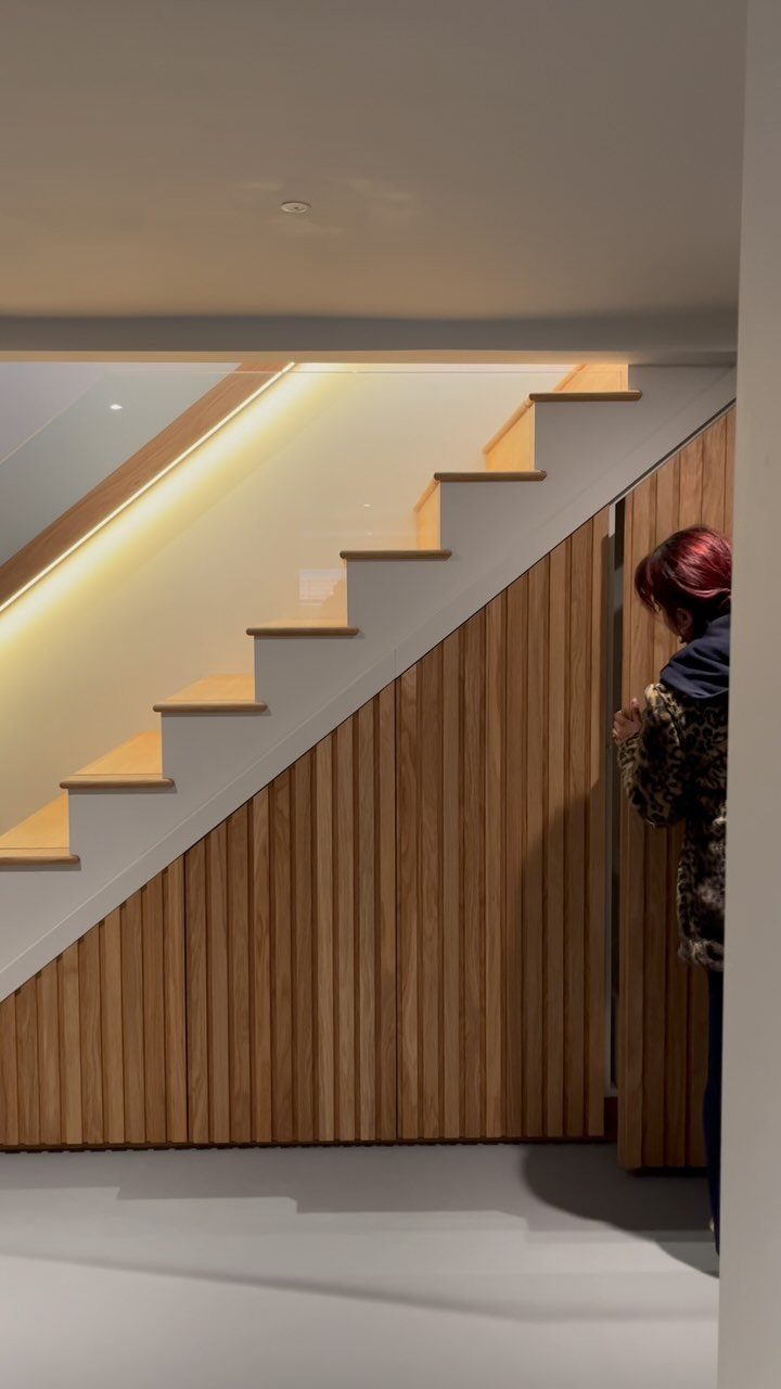 Hidden door under a modern staircase with wooden slat paneling and integrated lighting.