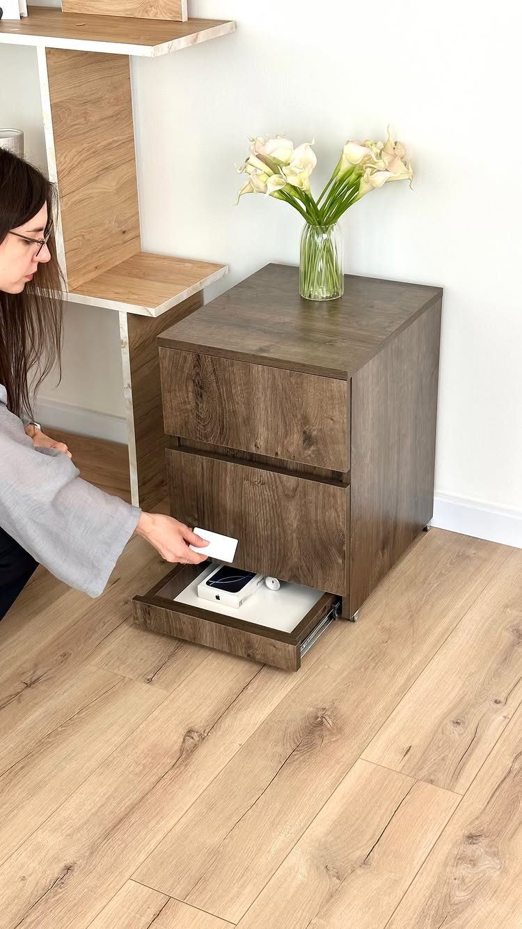 Hidden drawer at the base of a wood nightstand containing a smartphone.