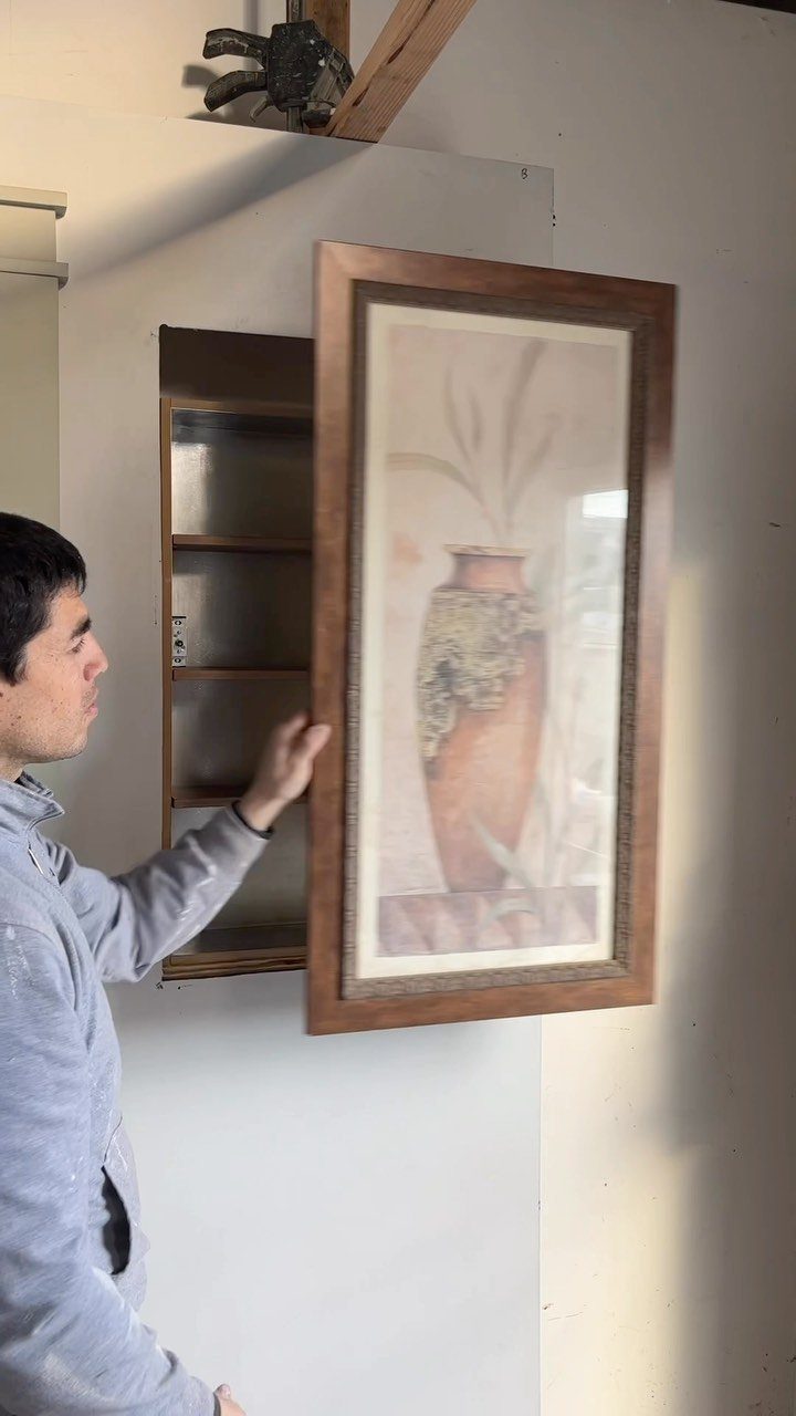 Man opening a framed wall picture to reveal a hidden wooden storage compartment.
